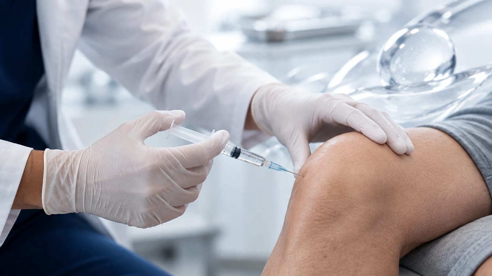 Médico de luvas aplicando uma injeção no joelho de um paciente